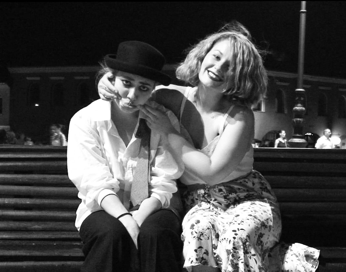 Two friends, one dressed as Chaplin, sitting on a bench at night