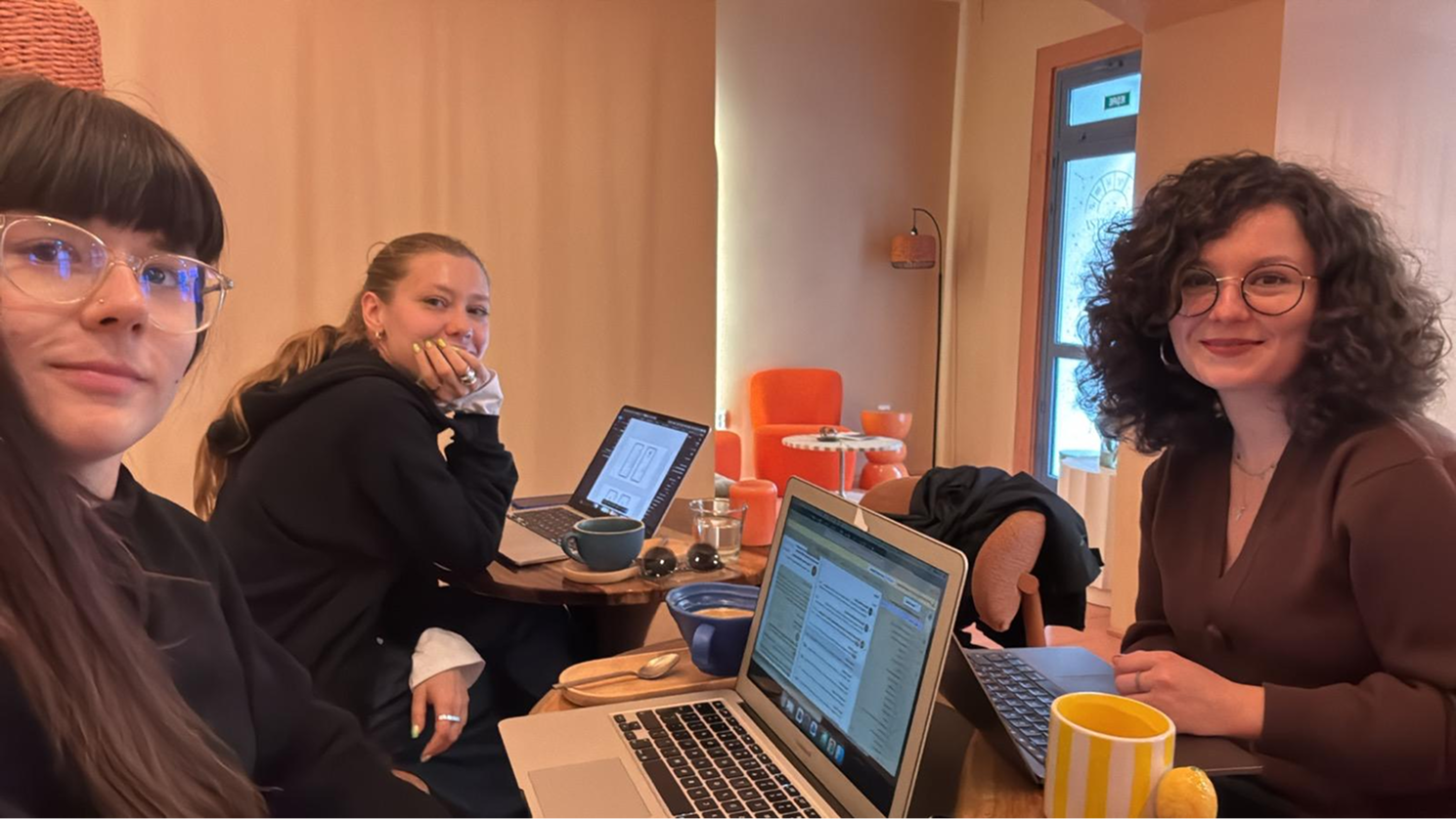Three friends around a café table, laptops, warm light